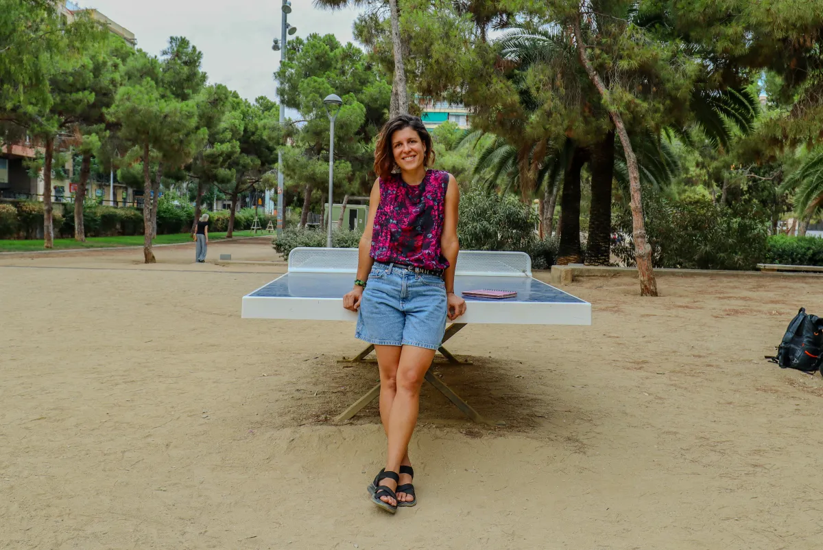 Emi leaning on a ping-pong table under pine trees, smiling