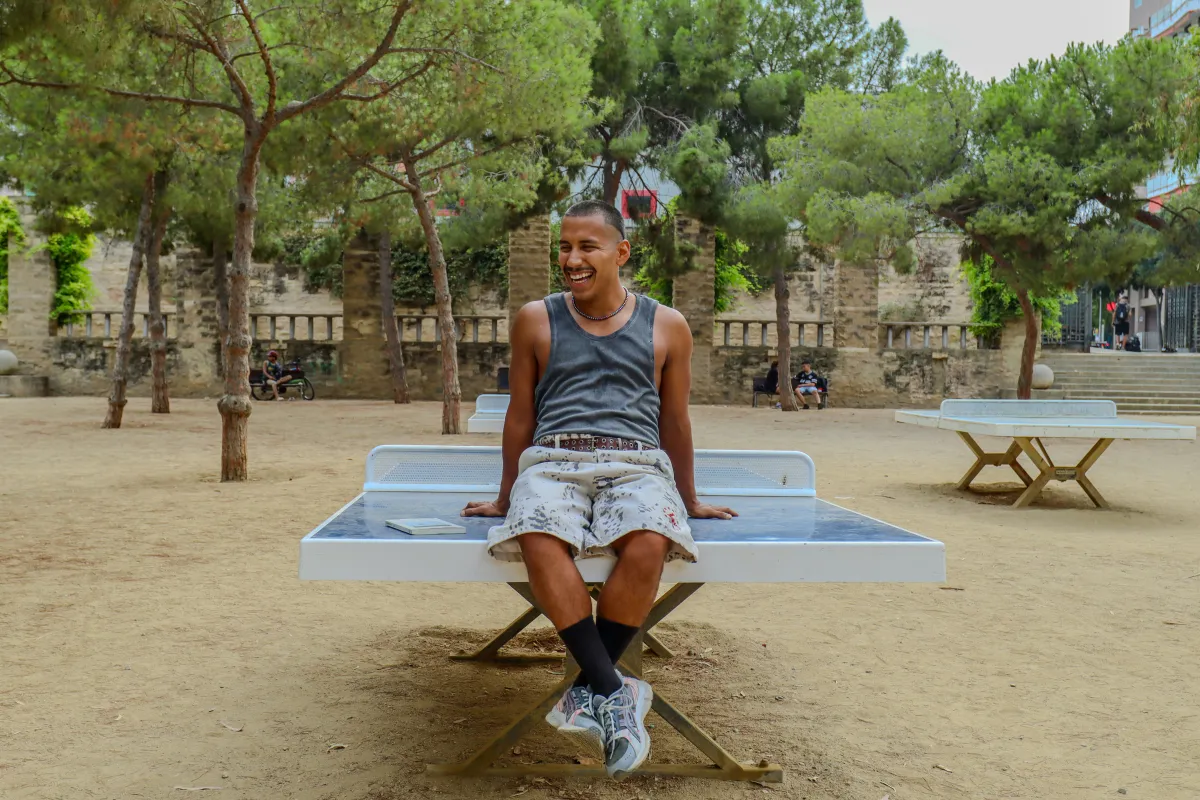 Nano sitting on a ping-pong table in a park, laughing
